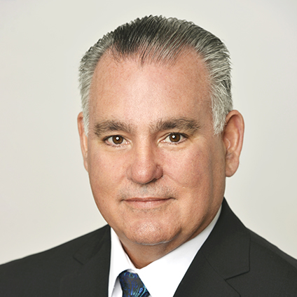 Headshot of a man with gray hair wearing a black suit and blue tie
