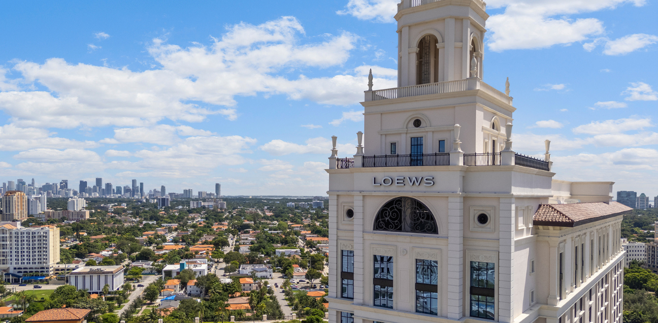 Photograph of the top of a white building located in the middle of houses and trees that surround it.